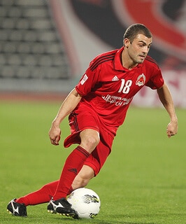 soccer player in red dribbling the ball