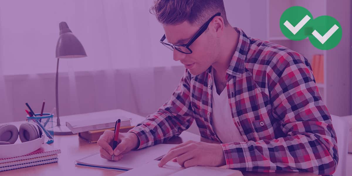 male passing student wearing glasses checks his ACT Percentiles in a book and prepares to write them on a notebook -image by Magoosh