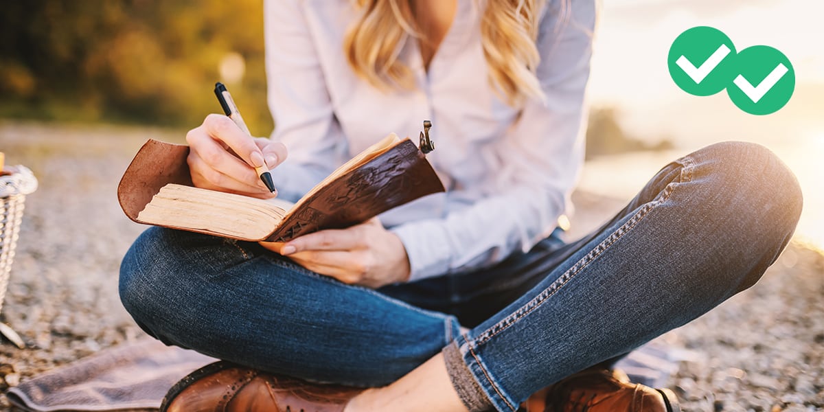 Woman with blond hair in jeans and a light blue blouse writing in a book