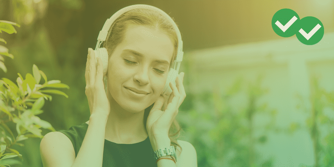 Woman with blonde hair holds headphones over her ears and closes her eyes as she listens to music