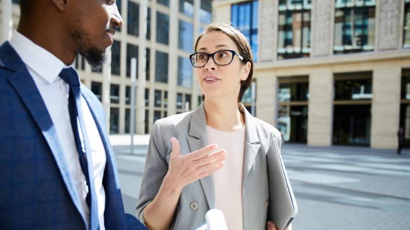 Woman in a business blazer and glasses explains herself to a man in a business suit