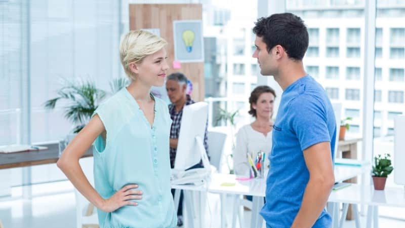 Woman in light blue shirt with hands on hip smiling at man in blue t-shirt who is talking to her, representing how to describe yourself as confident