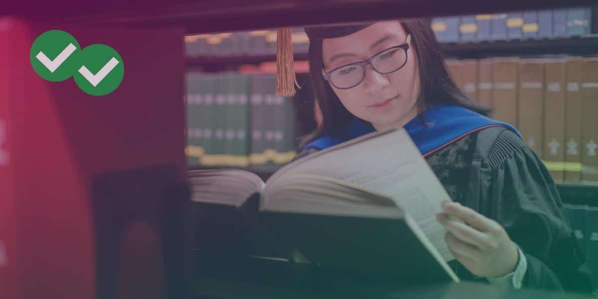 A student in a graduation gown reading a library book