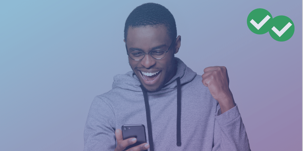 a student in glasses and a hoodie excitedly viewing phone with arm in mid-pump to represent good news from an act score report -image by magoosh