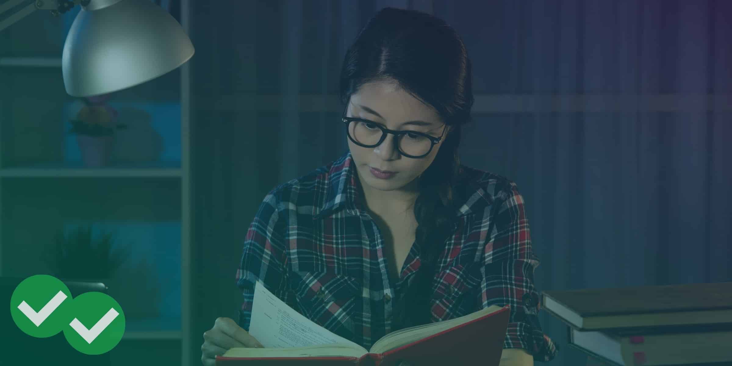 Woman wearing glasses and flipping through a book, with bookshelf and plants in the background, representing pulling a successful all-nighter - image by Magoosh