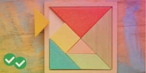 Wooden tetris board containing, red, blue, green, pink, and yellow shapes with one triangle pulled out, against a wooden background with paint splashes, symbolizing SAT prep games - image by Magoosh