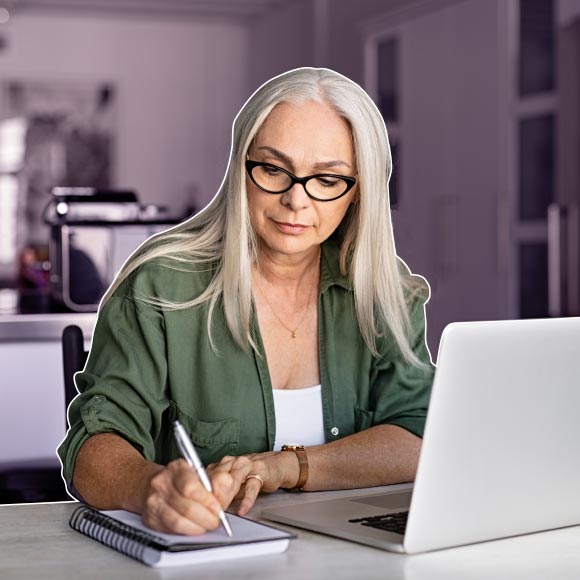 woman with long hair and glasses studying at dining room table