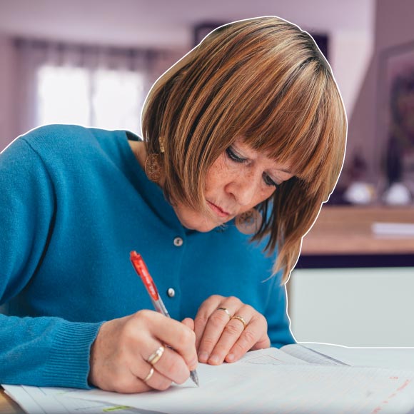 woman with brown hair and bangs writing in red pen