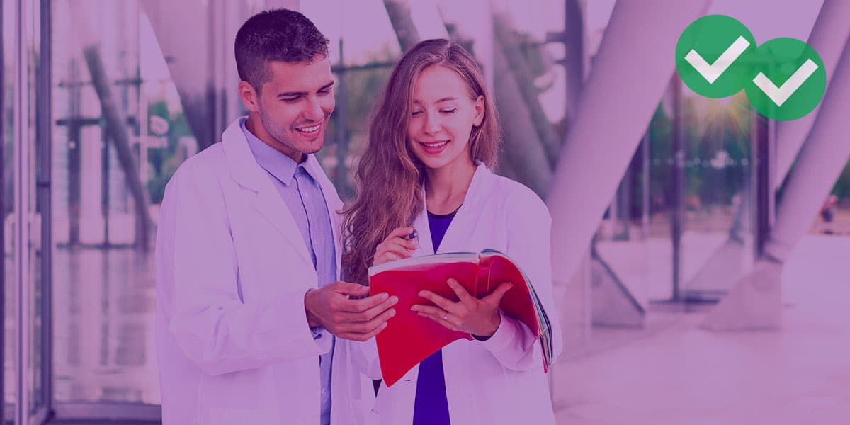 Two students in white coats looking at textbook