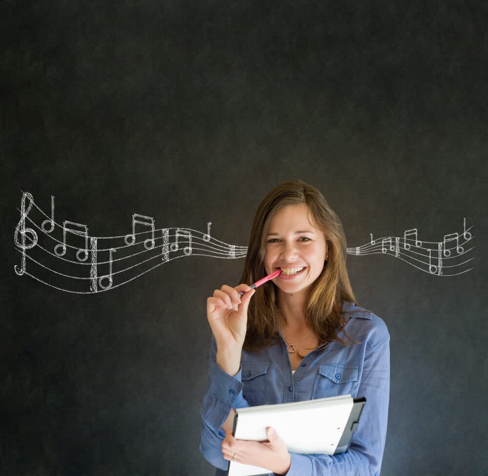 Teacher listens to fun teaching songs in front of a chalkboard